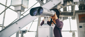 Woman looking through powerful binoculars at an industrial location suggesting discovery